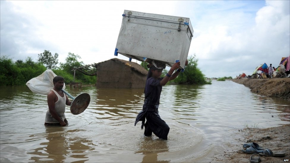 Villagers carry their belongings through flood water at Golarchi town in Badin district, about 200km east of Karachi