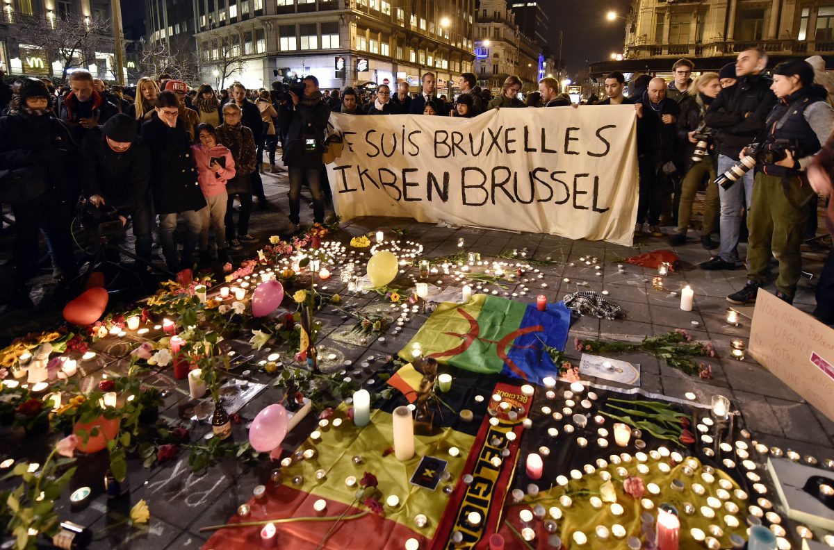 People holding a banner reading "I am Brussels" behind flowers and candles to mourn for the victims at Place de la Bourse in the center of Brussels, Tuesday, March 22, 2016. Bombs exploded at the Brussels airport and one of the city's metro stations Tuesday, killing and wounding scores of people, as a European capital was again locked down amid heightened security threats. (AP Photo/Martin Meissner)